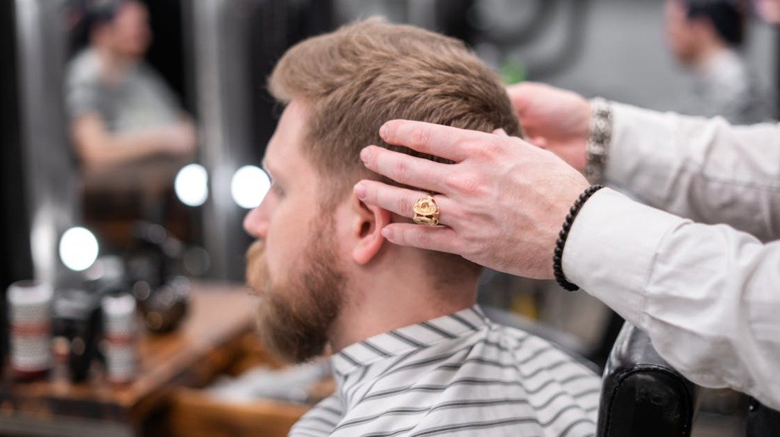 Homem com side part masculino ajustando o cabelo em frente ao espelho em ambiente sofisticado.
