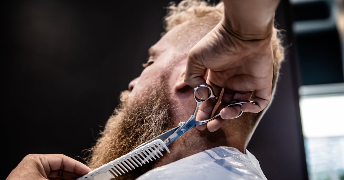 Homem alinhando barba curta com aparador em frente ao espelho