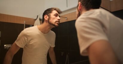 Homem analisando a barba no espelho durante rotina de grooming