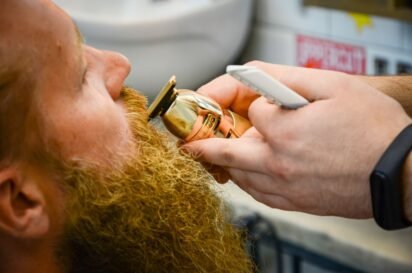 Barbeiro acertando o bigode e a barba de um cliente com aparador e pente