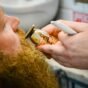 Barbeiro acertando o bigode e a barba de um cliente com aparador e pente