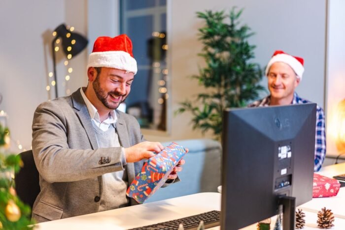 Homem de gorro de Papai Noel abrindo presente de amigo secreto no escritório