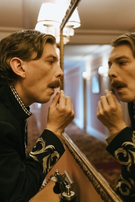 Homem de bigode ajeitando os pelos do rosto em frente ao espelho