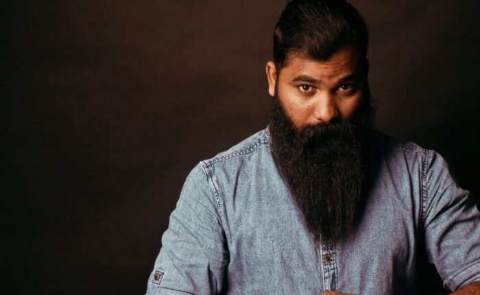 Homem com barba longa e cheia, bem penteada, em fundo escuro