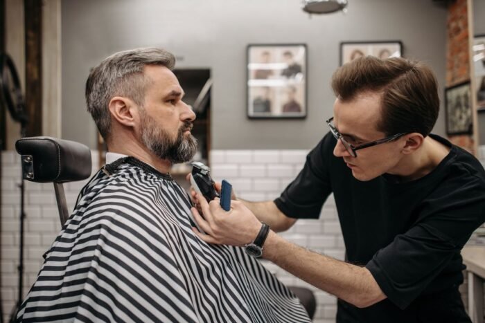 Barbeiro aparando a barba de um cliente com máquina na barbearia