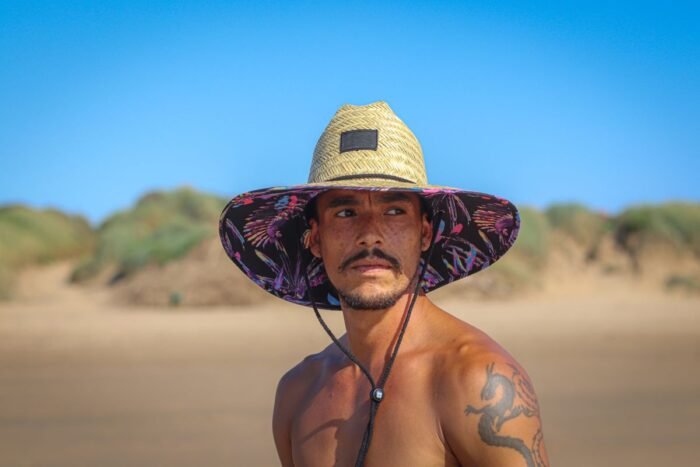Homem de bigode e chapéu de palha se protegendo do sol na praia