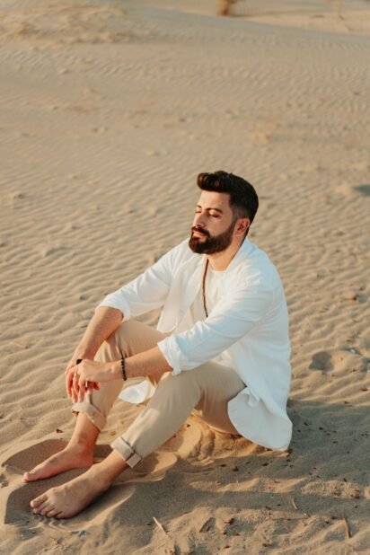 Homem de barba curta sentado na areia da praia em dia de verão