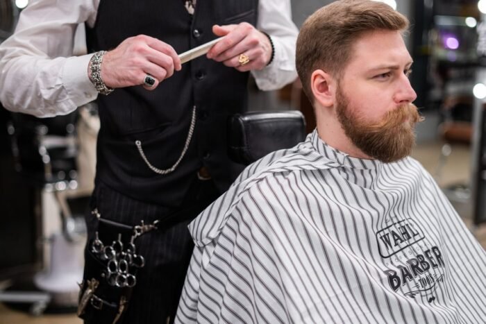 Barbeiro com pente na mão atendendo cliente de barba cheia na cadeira da barbearia
