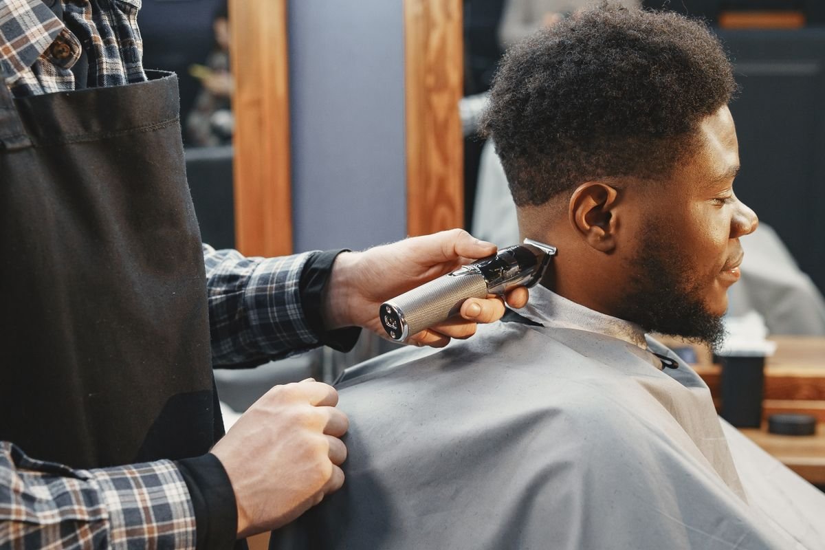 Barbeiro cortando a lateral do cabelo de um cliente com a máquina na barbearia