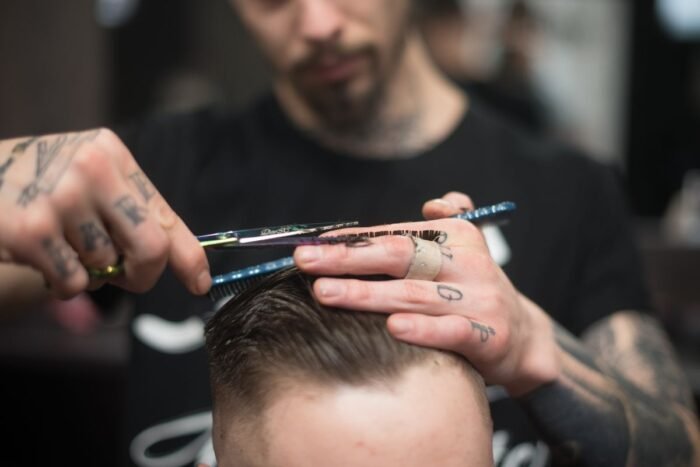 Barbeiro cortando com tesoura e pente o topo do cabelo de um cliente