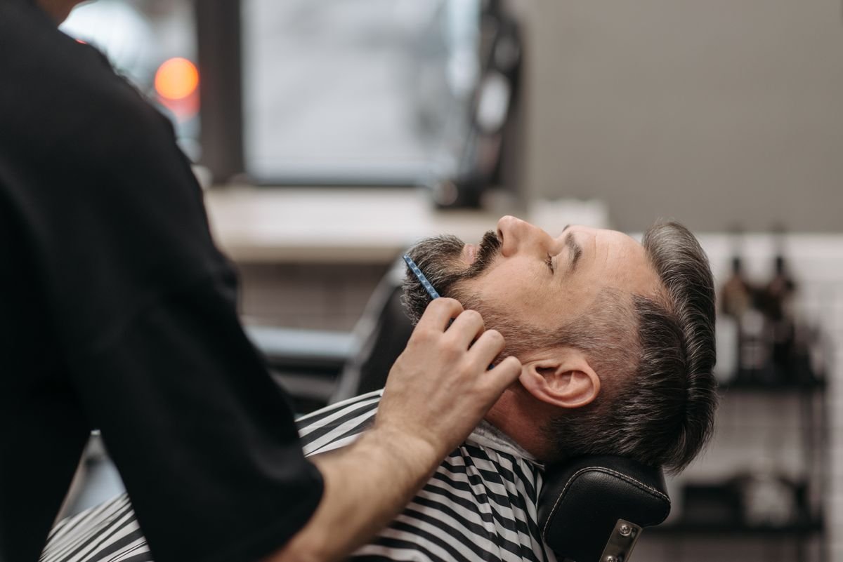 Barbeiro trabalhando na barba de um cliente reclinado na cadeira da barbearia