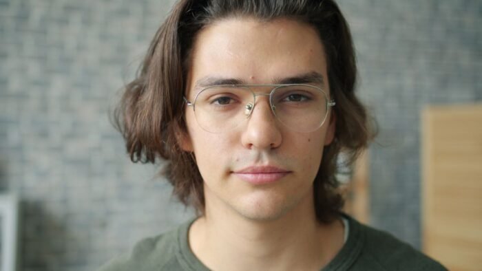 Jovem de óculos com cabelo médio repartido, com mechas emoldurando a testa