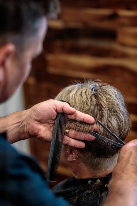 Barbeiro cortando o topo do cabelo com tesoura e pente na barbearia