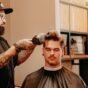 Barbeiro secando o cabelo de um cliente com secador para dar forma ao topo