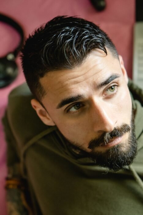 Homem com barba e corte curto de topo texturizado, com fios jogados para a frente