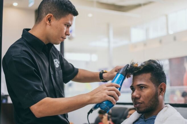 Barbeiro secando com secador o topo texturizado do cabelo de um cliente na barbearia