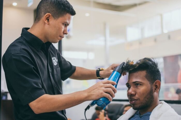 Barbeiro secando com secador o topo texturizado do cabelo de um cliente na barbearia