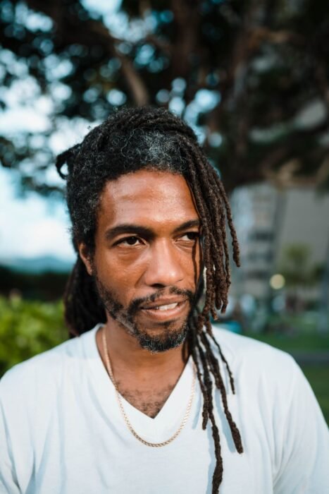 Homem com dreads longos e soltos e barba com contorno marcado, ao ar livre