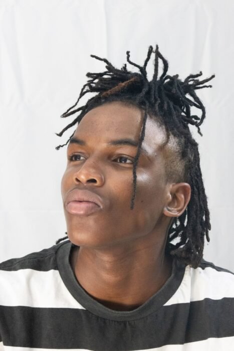 Jovem com dreads curtos e laterais baixas, em fundo branco