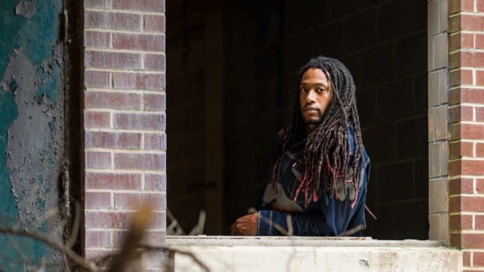 Homem com dreads longos e soltos caindo sobre os ombros, apoiado em uma janela
