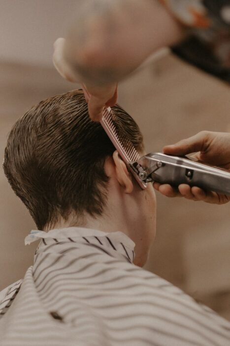 Barbeiro usando pente e máquina no topo do cabelo de um cliente