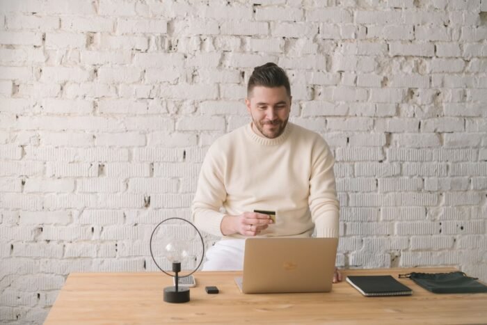Homem de barba segurando cartão de crédito enquanto compra pelo notebook
