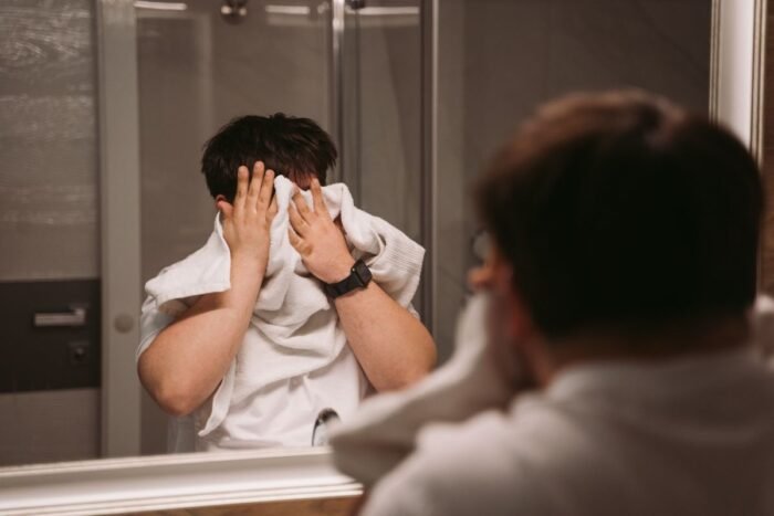Reflexo no espelho de um homem passando a toalha no rosto depois da limpeza