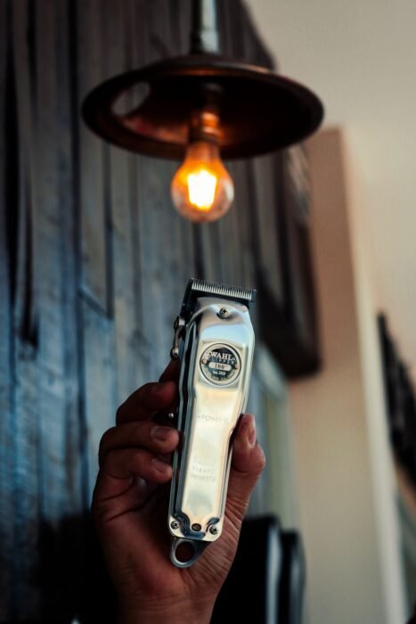 Mão segurando máquina de cortar cabelo metálica sob luz de luminária