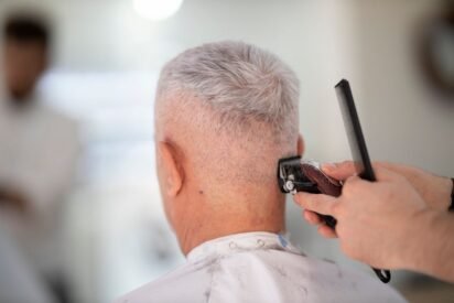 Barbeiro usando máquina de cortar cabelo no acabamento da nuca de um cliente grisalho