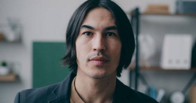 Homem com cabelo médio repartido ao meio, caindo para os dois lados do rosto