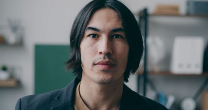 Homem com cabelo médio repartido ao meio, caindo para os dois lados do rosto