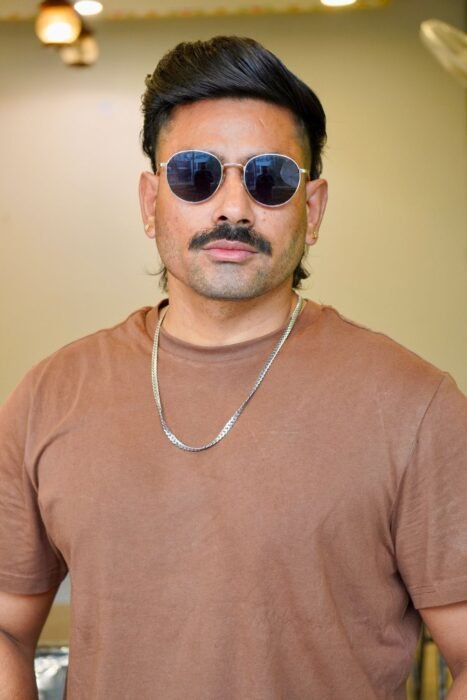 Homem de óculos escuros e bigode com mullet moderno, nuca mais longa e laterais curtas