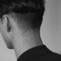 Nuca de um homem com cabelo curto e acabamento em degradê, vista de trás em preto e branco