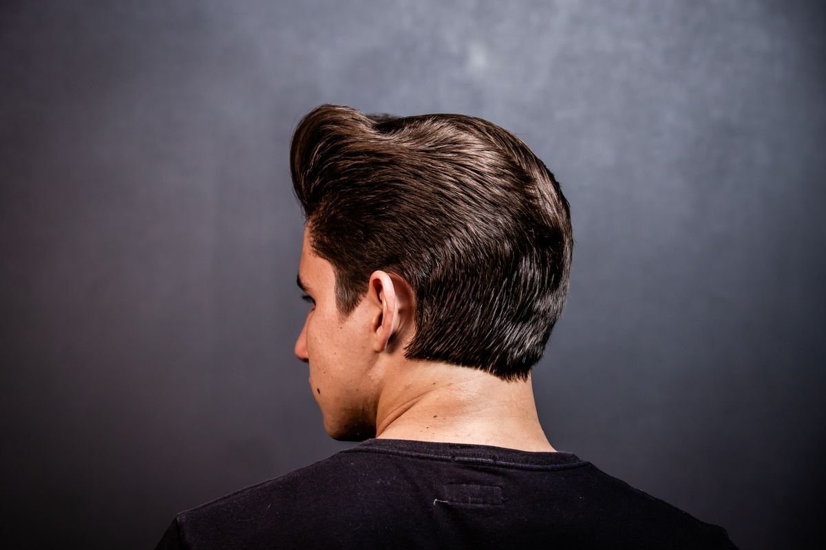 Homem de costas com cabelo médio penteado para trás e nuca com acabamento natural
