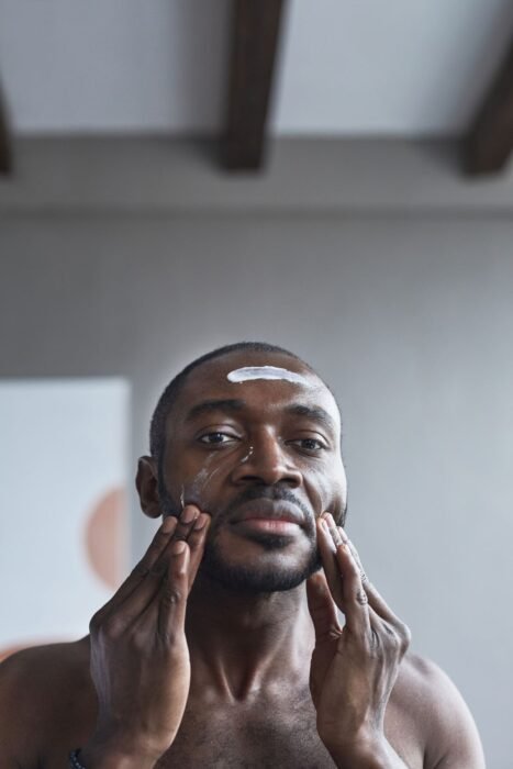 Homem aplicando camada fina de protetor solar facial em frente ao espelho