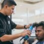 Barbeiro secando e modelando o topo do cabelo de um cliente com secador