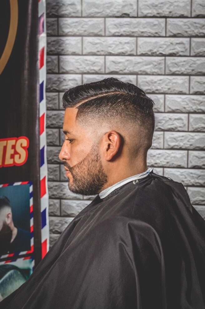 Homem de perfil na barbearia com laterais em taper fade e topo penteado de lado