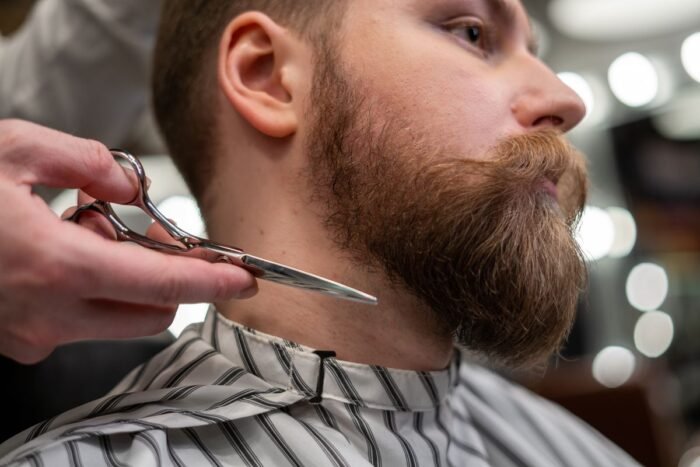 Barbeiro acertando o bigode e a barba de um cliente com tesoura