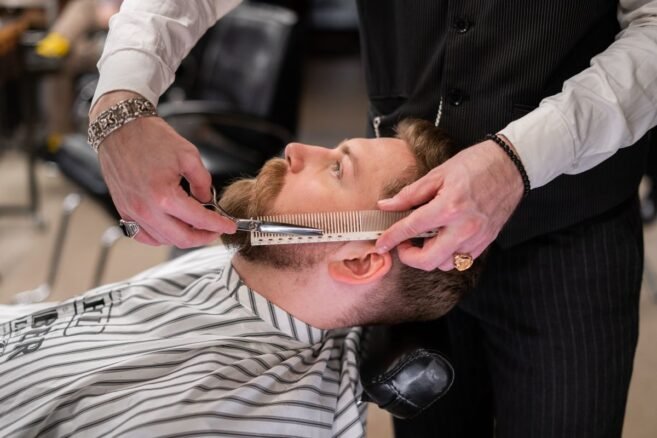 Barbeiro aparando a barba de um cliente com tesoura e pente