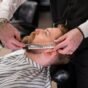 Barbeiro aparando a barba de um cliente com tesoura e pente